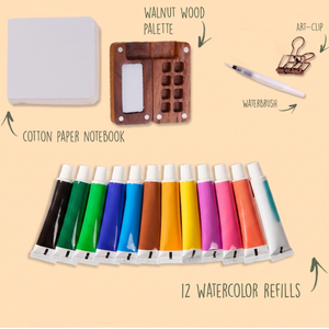 Set of watercolor refills with a palette, notebook, waterbrush, and art clip on a beige background.