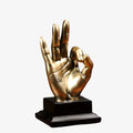A golden hand mudra statue with an antique finish, placed on a black base, displayed in a shop with various decorative items in the background.







