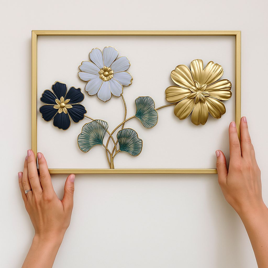 Rectangular gold frame displaying three metal flowers in white, black, and gold with delicate green leaves.

